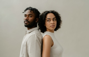 Black male and Hispanic woman standing back to back, looking away, in neutral tones